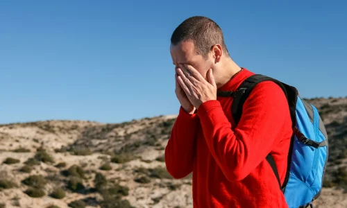 A hiker experiencing Altitude Sickness while trekking at high altitude, showing symptoms such as headache and fatigue in a mountainous landscape.